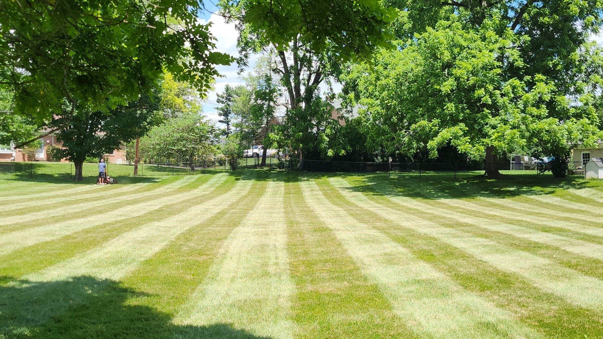 A freshly mown and striped lawn in front of a brick house, with a crew member finishing on a riding mower