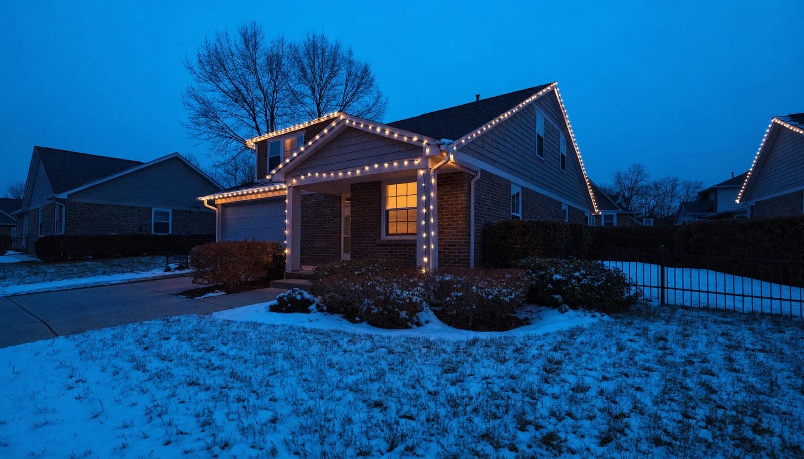 Illustration of a house at dusk with warm white lights running along the rooflines and porch, snow on the lawn