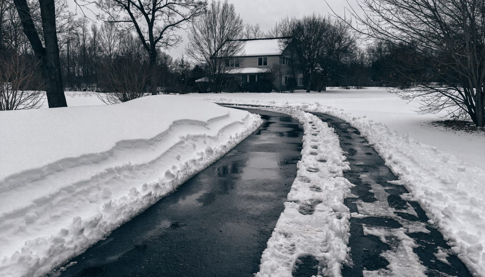 Illustration of a residential driveway cleared to bare asphalt after a snowstorm, with snow banked along both sides